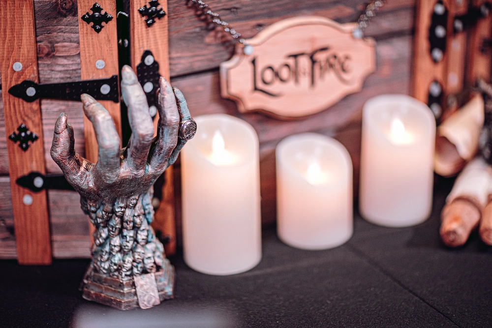 Escenografía de "El Apogeo del Mal" de Loot & Fire, con una mano esculpida, velas encendidas y fondo de madera, creando un ambiente de fantasía oscura.