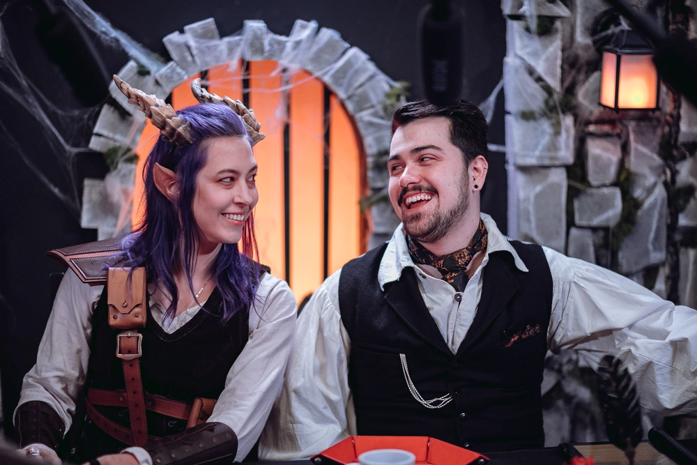 Los personajes Remus y Desdémona en el set de "El Apogeo del Mal" de Loot & Fire, compartiendo una sonrisa entre escenas.